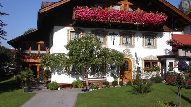 Ein traditionelles Chalet mit Holzbalkon, einem gepflegten Garten und blauem Himmel.
