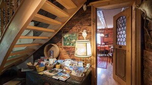 Ein rustikaler Raum mit einer Holztreppe, einem Tisch mit Postkarten, einer Lampe und einer Tür zu einem anderen Raum.