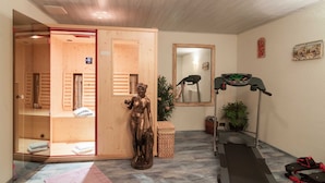 Ein Raum mit einer Holzsauna, einer Statue, einem Laufband und einem Spiegel.