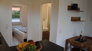 A compact room with a bed, a small table with a fruit bowl, a wooden chair, and a bottle of champagne on a small table. - Vacation apartment in Wackerballig/Gelting 200m to the beach - Holiday apartment (Gelting)
