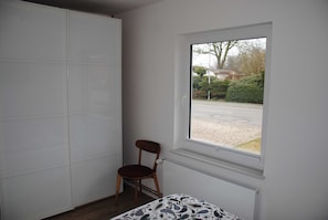 Une pièce avec une grande fenêtre, un radiateur, une chaise et une armoire.