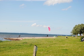 Une zone herbeuse avec une plage et une étendue d’eau en arrière-plan.