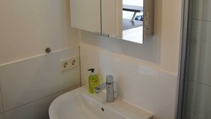 A bathroom with a white sink, a mirror, and a glass shower enclosure. - Vacation apartment in Wackerballig/Gelting 200m to the beach - Holiday apartment (Gelting)