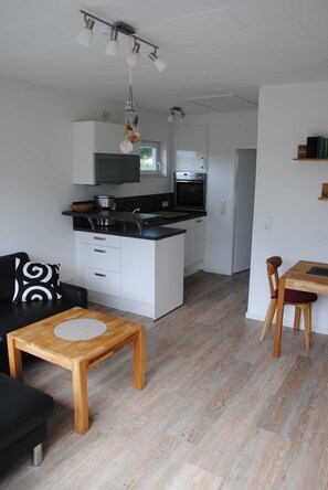 Una cocina moderna con armarios blancos, encimera negra y mesa de comedor de madera.