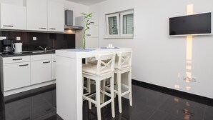 Une cuisine moderne avec des meubles blancs, un plan de travail noir et un petit coin repas avec des chaises blanches.