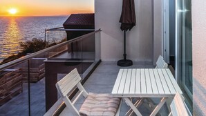 Un balcon avec une table et des chaises, d’où l’on peut admirer le coucher de soleil sur la mer.