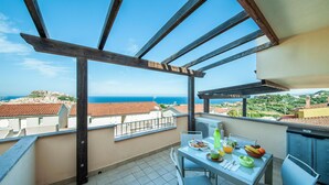 Ein Balkon mit einem Frühstückstisch, mit Blick auf eine Küstenstadt und das Meer.