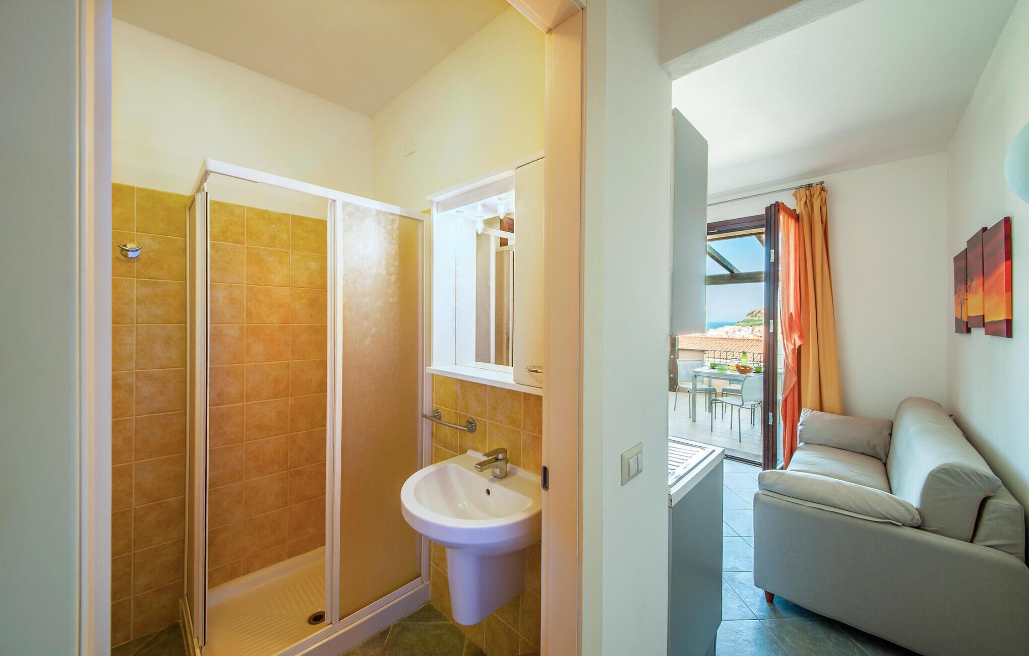 Une salle de bain avec douche, lavabo et vue sur un balcon équipé d’une table et de chaises.