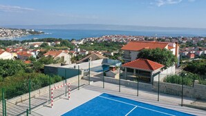 A residential area with a blue tennis court, surrounded by houses with red roofs, and a view of the sea and distant hills. - Stunning apartment in Split (Split)