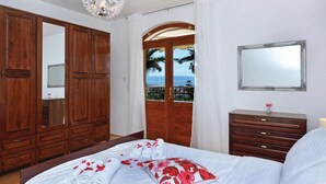 A bedroom with a bed, a wooden wardrobe, a dresser, a mirror, and a view of the sea through a door. - Stunning apartment in Split (Split)