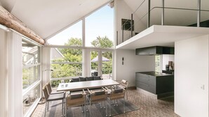 Eine moderne Küche mit einer großen Kochinsel, einem Essbereich mit Tisch und Stühlen und Blick ins Freie durch große Fenster.
