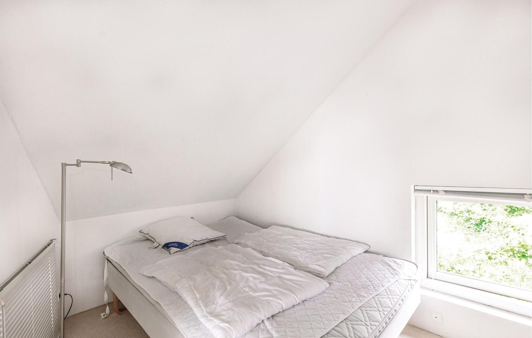 A small, white, sloped ceiling bedroom with a single bed, a bedside table, and a window.