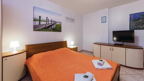 Ett hotellrum med en säng, en tv, ett skrivbord och en vägg med en tavla som föreställer en brygga och ordet ”HEM”.