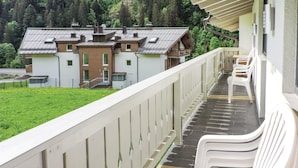 A balcony with white plastic chairs, a view of a building with a sloped roof, and a grassy area in the background.
