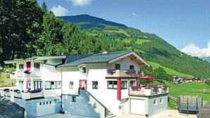 A two-story building with a balcony, a swimming pool, and a view of a green valley and mountains.