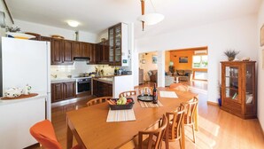 A modern kitchen with wooden cabinets, a dining table with chairs, and a kitchen island. - Beautiful home in Okrug Gornji (Okrug Gornji)