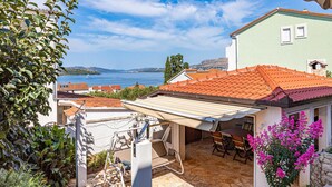 A patio with outdoor furniture, a view of a lake, and a building with a red-tiled roof. - Beautiful home in Okrug Gornji (Okrug Gornji)