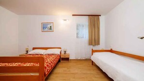 Una habitación con dos camas de madera, una mesita de noche con lámpara, un cuadro en la pared y una ventana con cortinas.