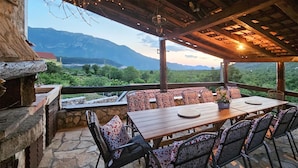 Une terrasse extérieure avec une table et des chaises en bois, un sol en pierre et une vue sur les montagnes.