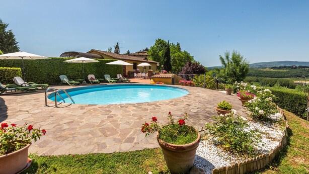 Une piscine entourée de chaises longues et de parasols, agrémentée de plantes en pot et offrant une vue sur la campagne.