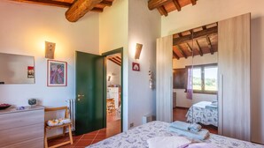 Une chambre à coucher comprenant un lit, une commode, une chaise, une porte donnant sur une salle de bain et une vue sur l’extérieur.