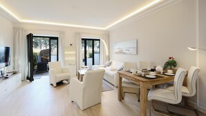 A modern living room with a dining area, white furniture, a TV, and a large window with curtains. - Pet friendly apartment in Binz with WiFi (Prora/Rügen)