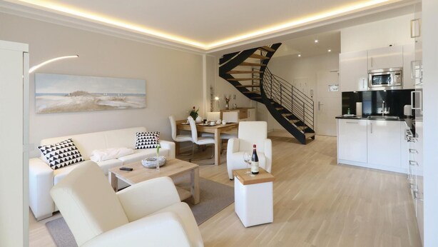 A modern living room with a white sofa, a dining area, and a kitchen.
