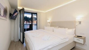 A hotel room with a bed, bedside tables, a TV, and a view of trees through a window.
