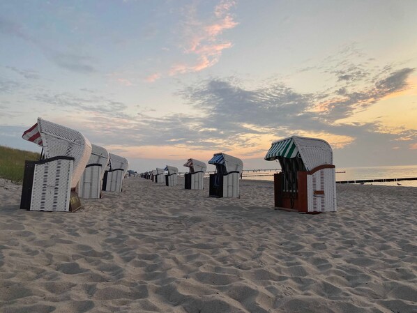 A beach with rows of beach huts and a pier in the background.