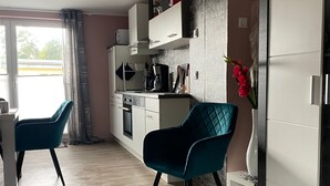 Ett modernt kök med vita skåp, en matplats med turkosa stolar och en vit lykta på golvet.