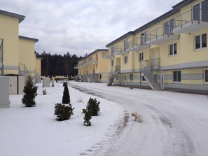 A snow-covered street with multi-story buildings, a staircase, and a small dog. - *der Strandkater OG / DG Priemer GM 69667 - der Strandkater SNR: 66 (Gelbensande)