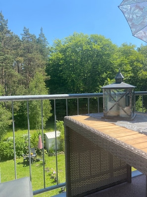 Un balcón con muebles de mimbre, un farol de cristal y vistas a un jardín con árboles y una mesa con sillas.