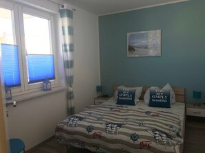 Un dormitorio con cama, dos mesitas de noche, una ventana con persianas y cortina, y un cuadro colgado en la pared.