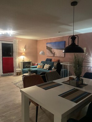 Ein Wohnzimmer mit einer Couch, einem Esstisch, einer Lampe und einem Gemälde an der Wand.