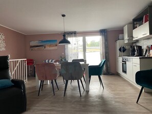 A modern kitchen with white cabinets, a dining area with a table and chairs, a large window with curtains, and a ceiling fan. - *der Strandkater OG / DG Priemer GM 69667 - der Strandkater SNR: 66 (Gelbensande)