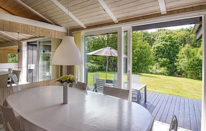 Ein moderner Essbereich im Freien mit einem runden Tisch, Stühlen, einer Lampe und Blick auf einen üppigen Garten.