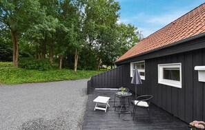 Ein schwarzes Gebäude mit rotem Ziegeldach, einem Kiesweg und einer kleinen Außen-Sitzgelegenheit mit Tisch und zwei Stühlen.