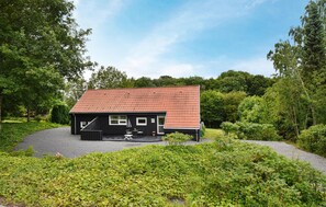 Ein kleines, eingeschossiges Haus mit rotem Ziegeldach, umgeben von üppiger Vegetation und Bäumen.