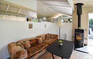 A modern living room with a patterned sofa, a black table with a vase, a fireplace, and a high ceiling with wooden beams. - 3 bedroom awesome home in Asperup (Asperup)