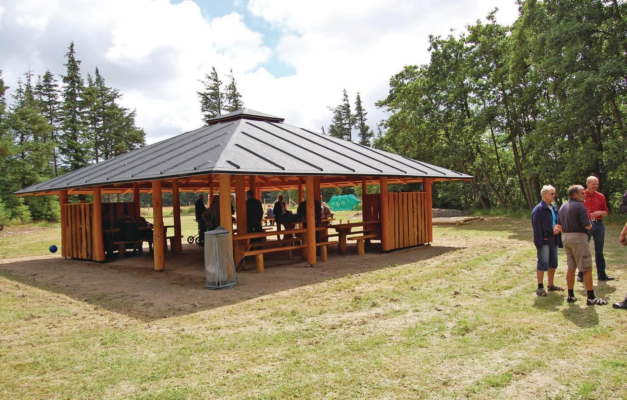 A wooden pavilion with a metal roof, benches, and a trash can.