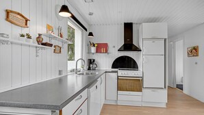 Une cuisine moderne avec des meubles blancs, un plan de travail en acier inoxydable, une hotte noire et un four encastré.
