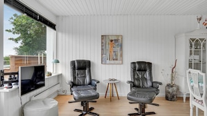 Une pièce comprenant deux fauteuils en cuir noir, une petite table, un tableau accroché au mur et un téléviseur posé sur un meuble.