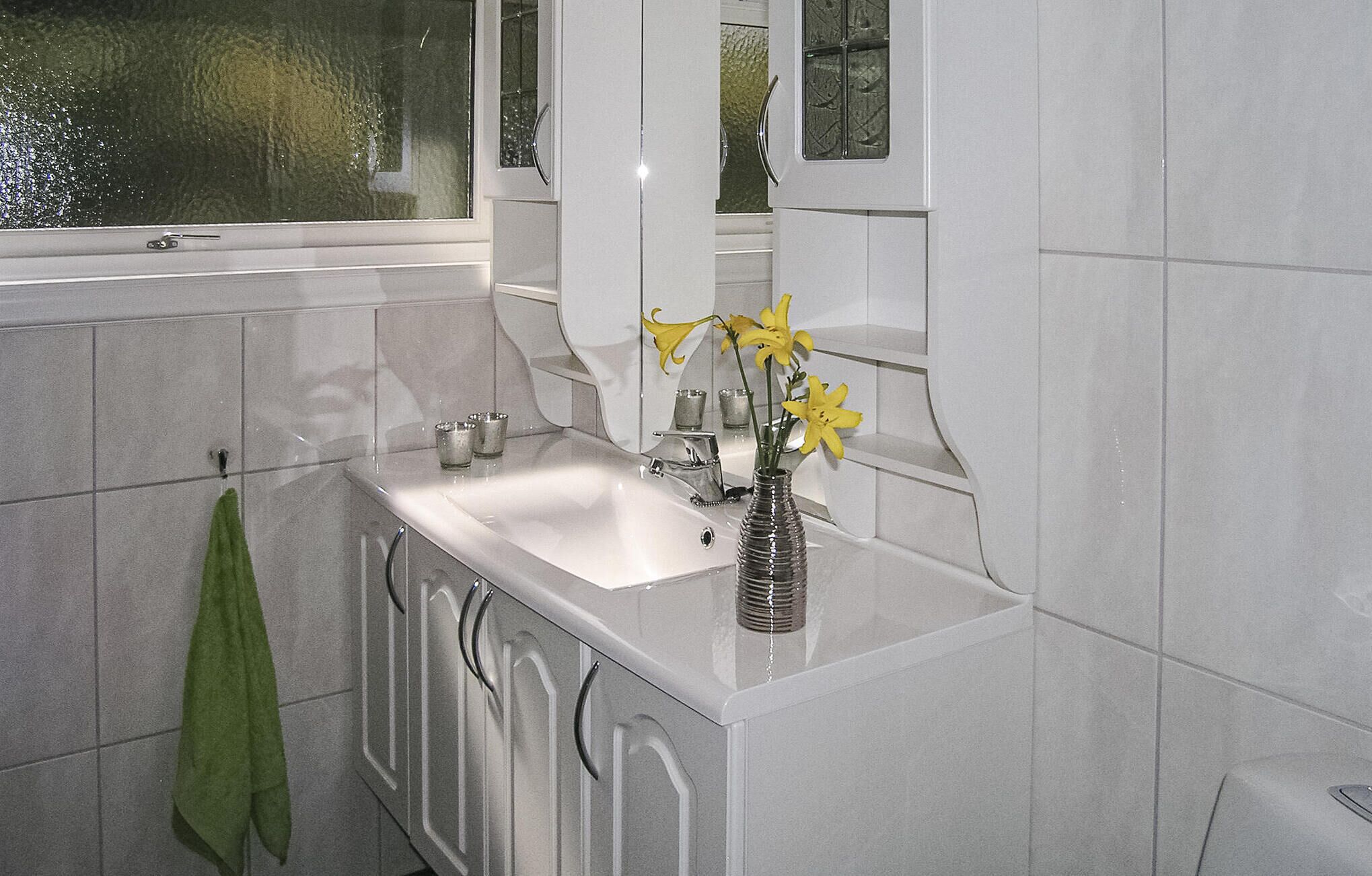 Un baño con un lavamanos blanco, una toalla verde y un florero con flores amarillas.
