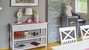 Una habitación con una consola blanca, libros, una lámpara y una pared de piedra.