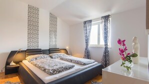 Ein modernes Schlafzimmer mit einem großen Bett, einem Nachttisch, einer Lampe und einem Fenster mit gemusterten Vorhängen.