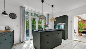 A modern kitchen with a central island, black cabinets, and a large window.