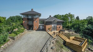 A two-story building with a prominent tower, a covered outdoor seating area, and a gravel driveway leading to the entrance.