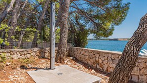Un mur de pierre avec un poteau métallique et une zone pavée à proximité d’une étendue d’eau.