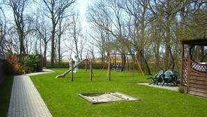 Ein Spielplatz mit Rutsche, Schaukeln und einer kleinen Spielhütte.