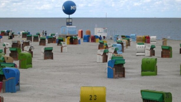 Ein Strand mit zahlreichen nummerierten Behältern, einem Rettungsturm und freiem Blick auf das Meer.